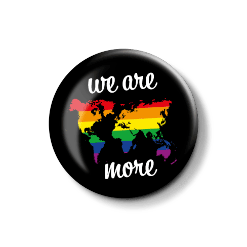**Title-Text**: Anstecknadel mit Regenbogen-Weltkarte und Motto "we are more". **Alt-Text**: Bunte Anstecknadel mit einer Weltkarte in Regenbogenfarben und dem Schriftzug "we are more".